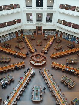 An ornate library interior with large reading tables and bookshelves, viewed from above.