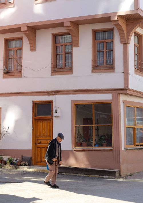 Free Elderly man walking with a cane past a traditional stucco house in the daytime. Stock Photo