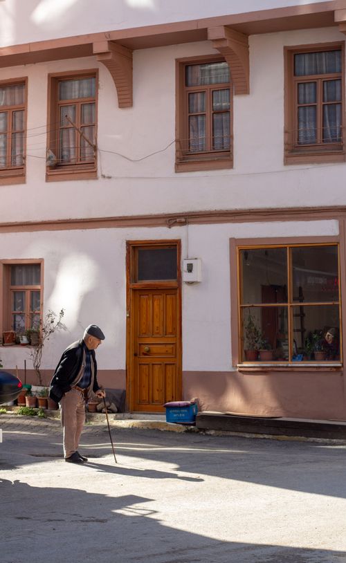 Free An elderly man walks with a cane past a charming urban building. Natural lighting enhances the scene. Stock Photo