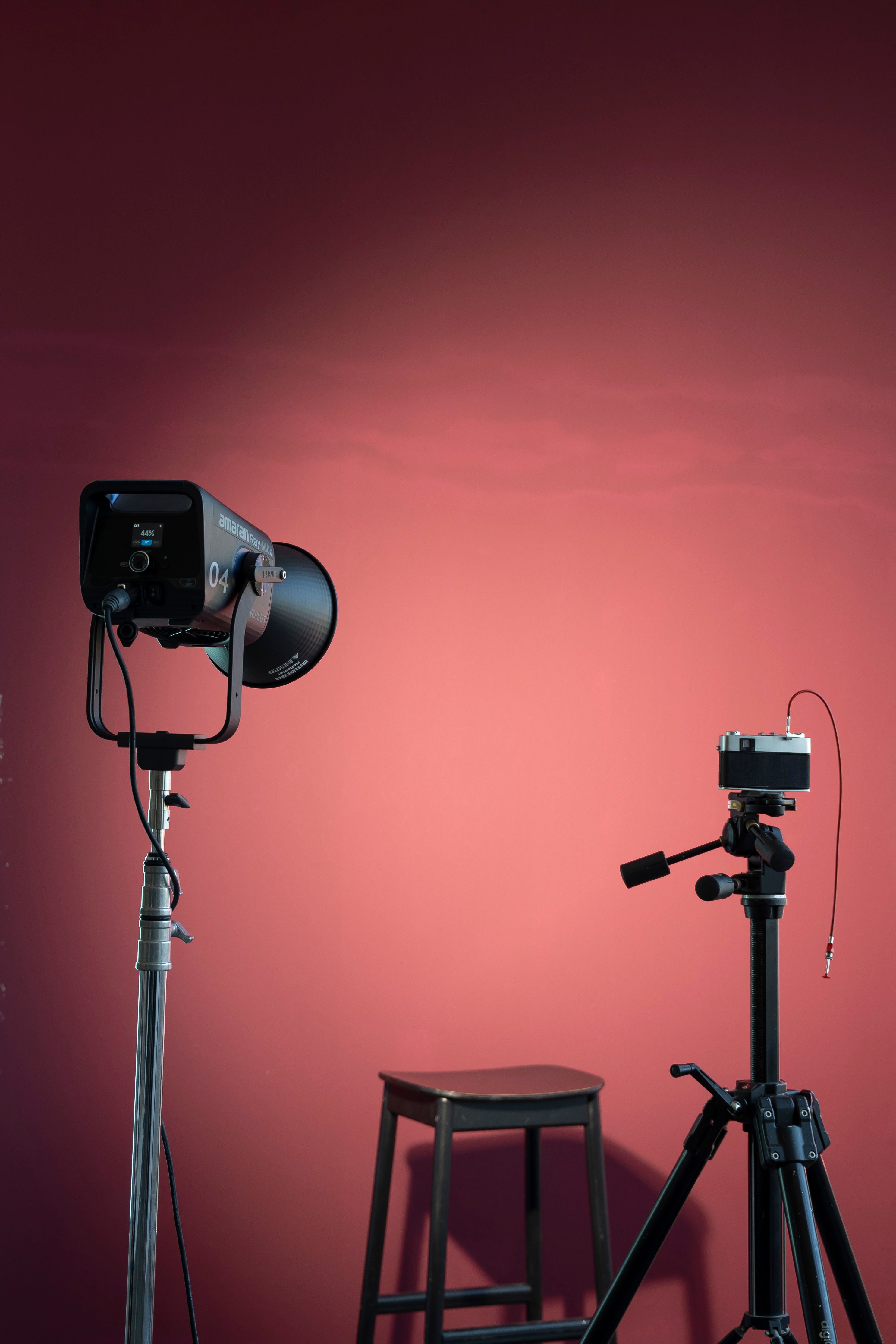 Studio lighting and camera setup with a stool against a red backdrop.