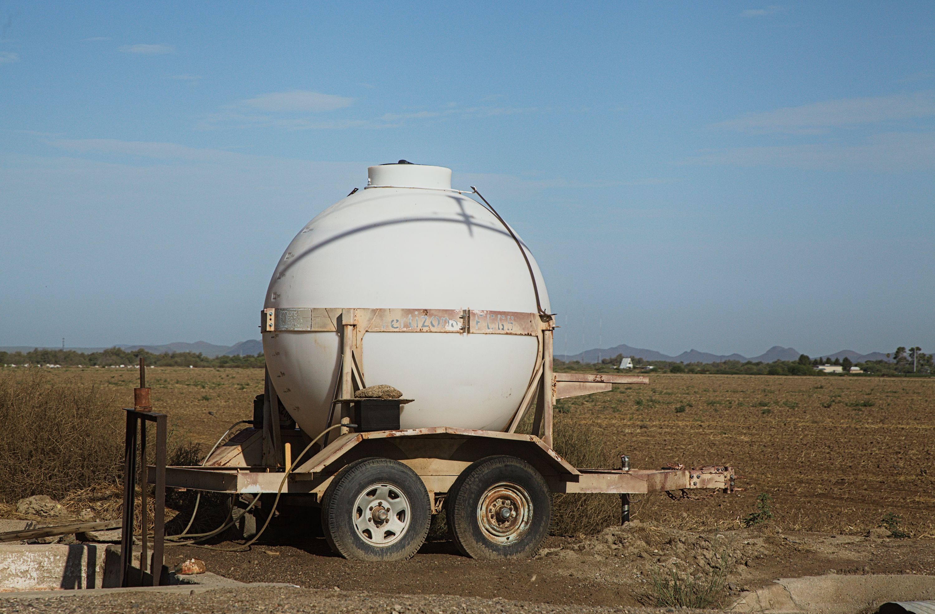 Fotomural Un tanque de agua redondo sobre un remolque, ubicado en un campo rural bajo un cielo azul despejado.