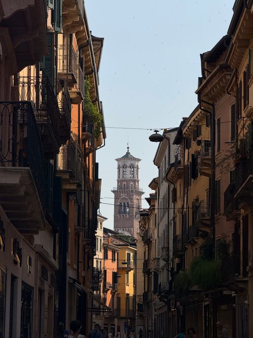 Free Picturesque Italian street with colorful buildings and a historic bell tower in the distance. Stock Photo