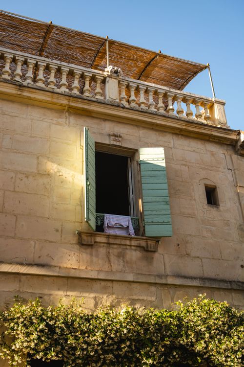 Free Sunlit facade with open shuttered window in Arles, France. Stock Photo