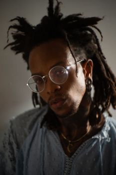 Moody portrait of an individual with dreadlocks and glasses in soft lighting.