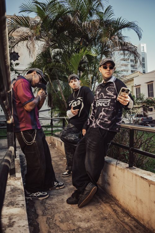 Free Three young adults in urban streetwear pose in an outdoor setting with palm trees. Stock Photo