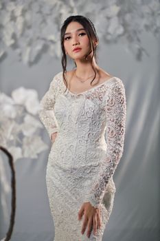 Portrait of an elegant woman in a lace wedding dress posing indoors with artistic background.