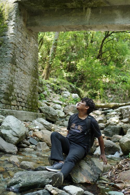 Free Man sitting on rocks under a bridge in Gopeshwar, India, enjoying the forest scenery. Stock Photo