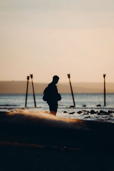 Captivating silhouette of a man strolling along a tranquil beach at sunset, evoking a serene and introspective mood.