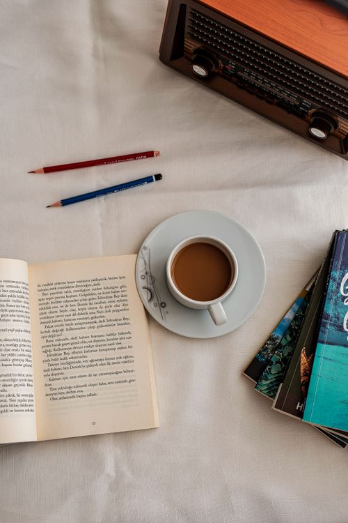 Free Top view of an inviting reading setup with coffee, books, and vintage radio on a white tablecloth. Stock Photo