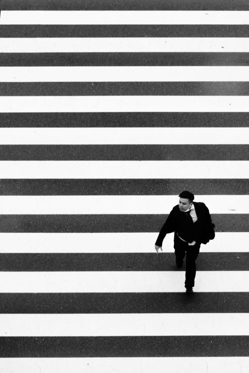 Free A lone man crossing a zebra crossing in a black and white urban setting. Stock Photo