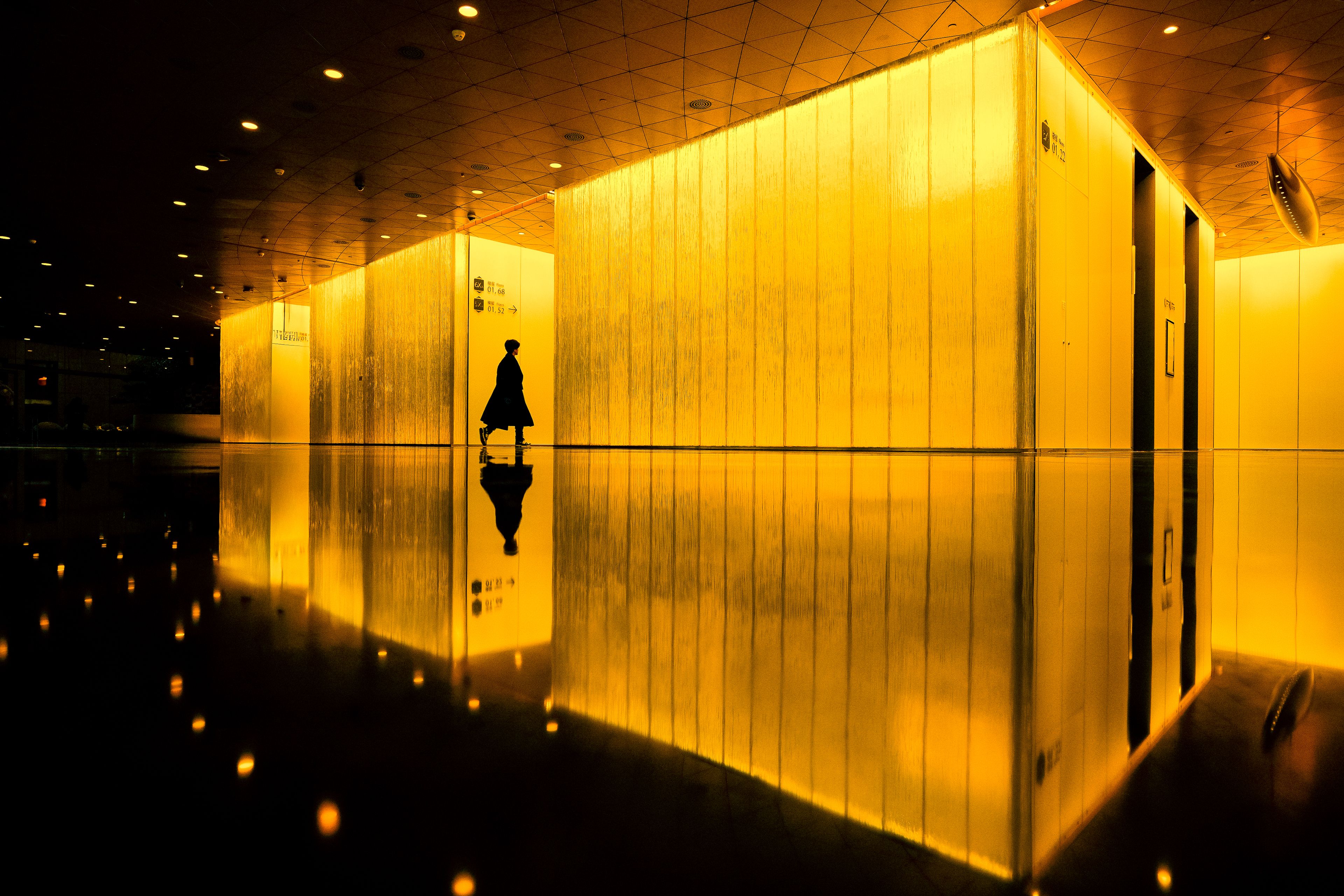 A silhouette of a person against illuminated yellow walls creates a dramatic urban reflection in a modern setting.