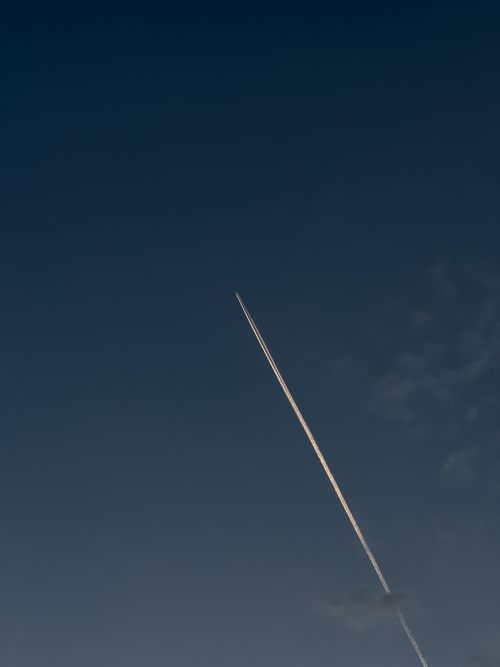 Free A white jet contrail cuts through a deep blue sky, leaving a linear cloud trail. Stock Photo