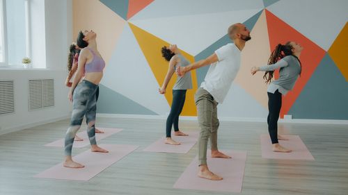Free A group of adults engaging in a yoga class indoors with a colorful geometric wall. Stock Photo