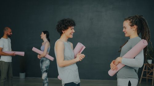 Free Four adults in a yoga class indoors, chatting and holding mats, promoting wellness. Stock Photo