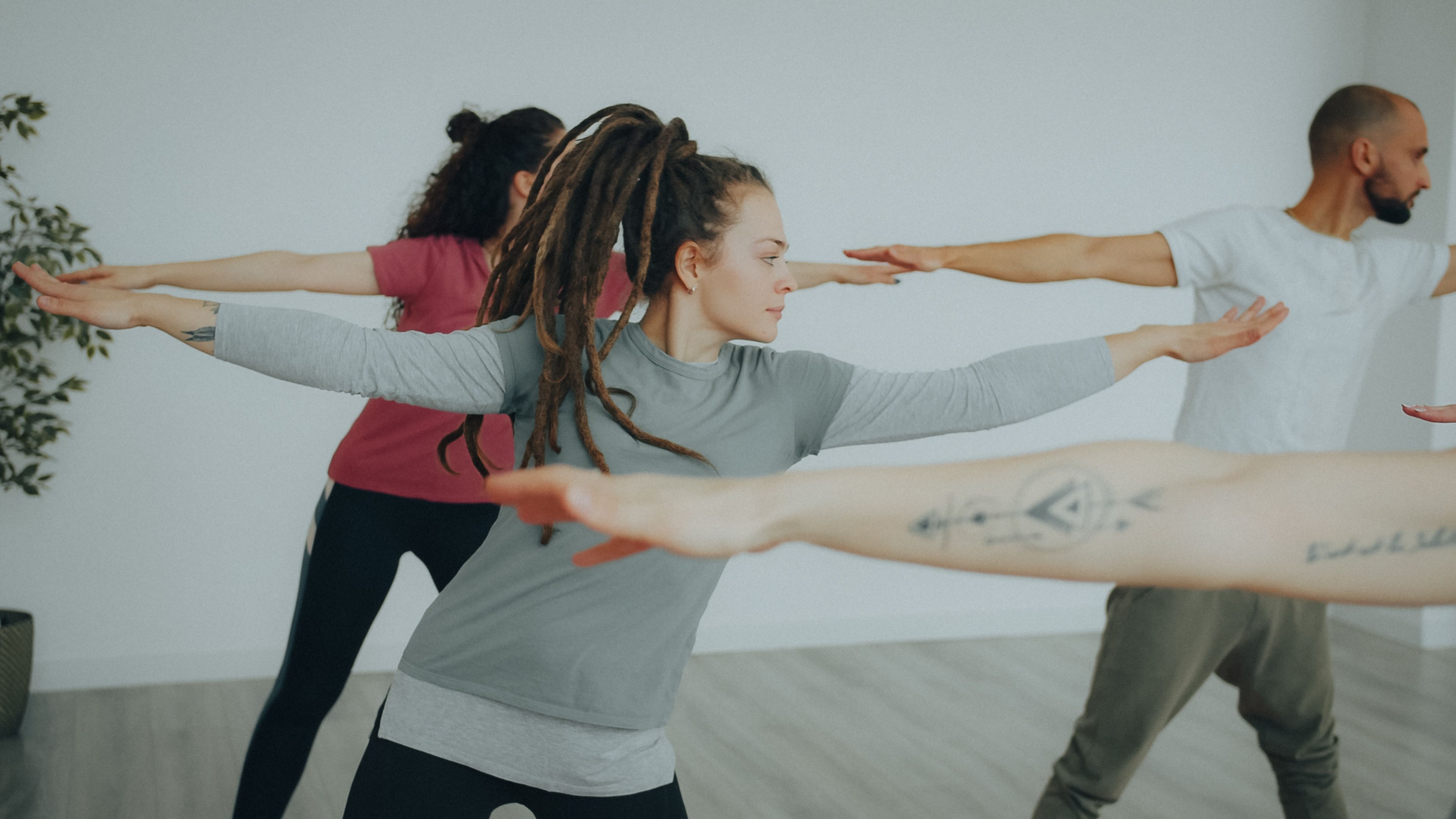 Adults practicing yoga in a bright room, focusing on balance and mindfulness through warrior pose.