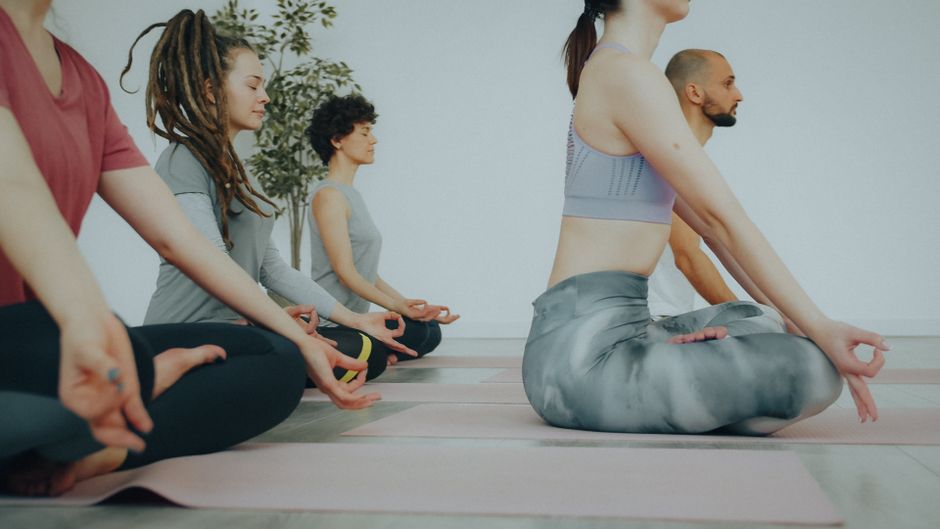A diverse group of people practicing meditation in a yoga class indoors.