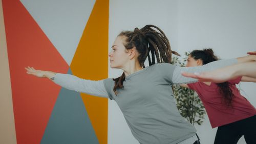 Free Women performing yoga in a modern indoor studio with colorful geometric walls. Stock Photo