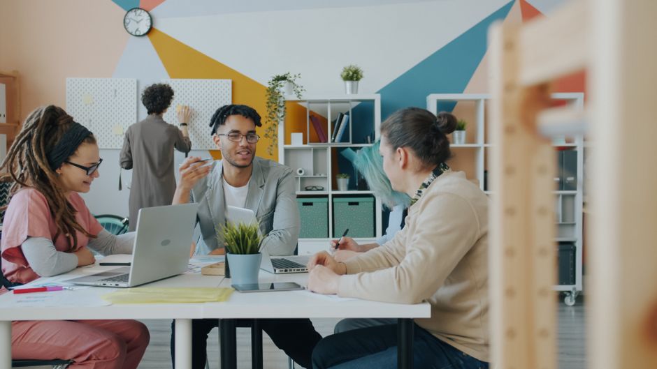 Diverse group collaborating in a bright, modern office environment with laptops and plants.