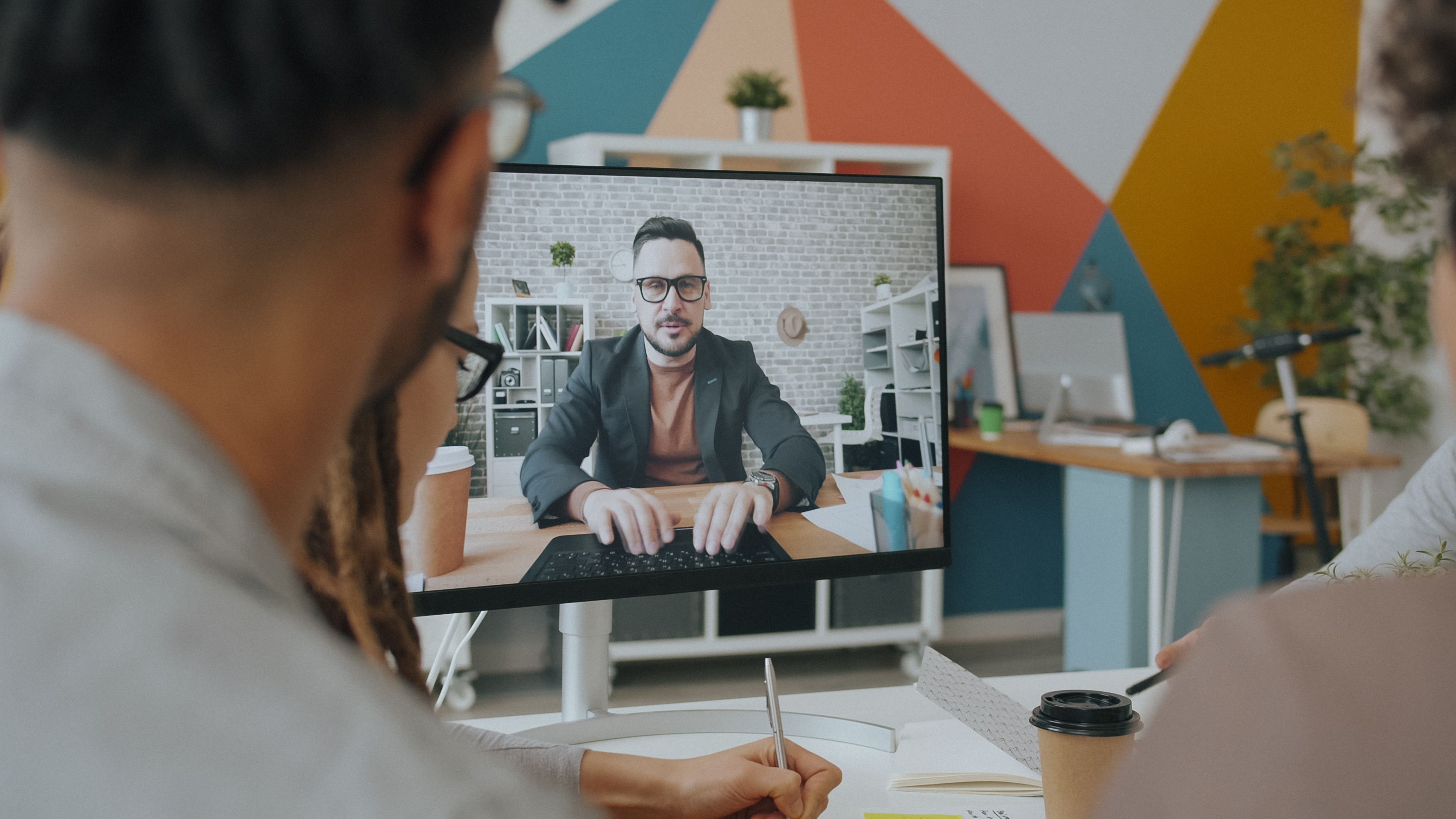 A team engages in a video conference call with a colleague over a computer screen in a colorful office.