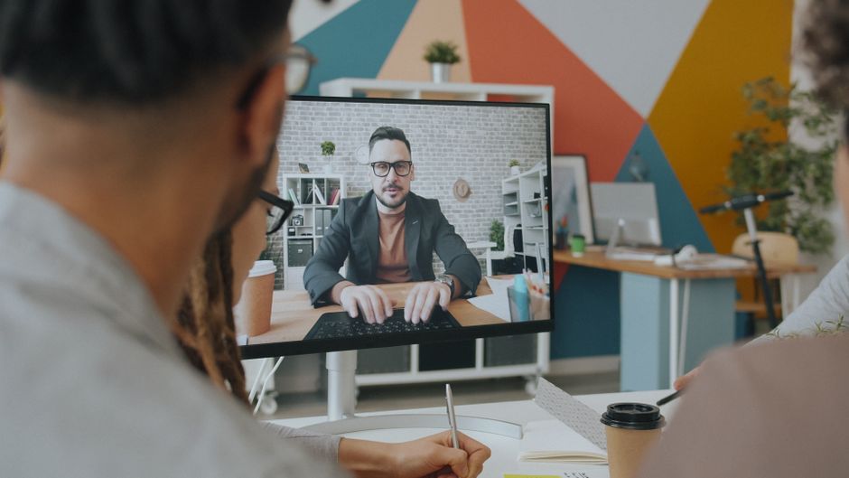 A team engages in a video conference call with a colleague over a computer screen in a colorful office.