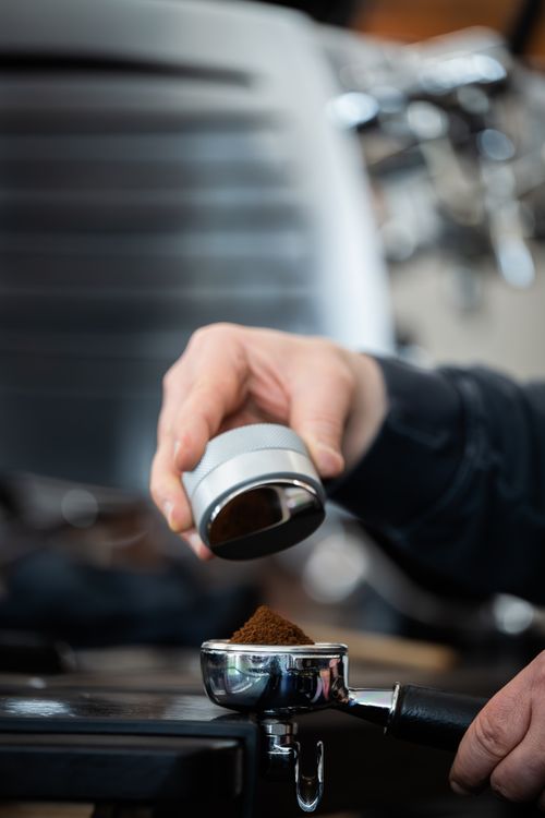 Free Close-up of a barista tamping ground coffee into an espresso machine portafilter. Stock Photo