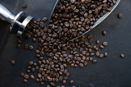 Free A detailed view of roasted coffee beans spilling from a scoop on a black surface. Stock Photo