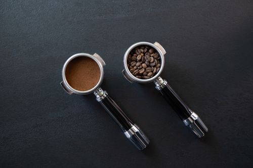 Free Overhead shot of espresso portafilters with coffee beans and grounds on black surface. Stock Photo