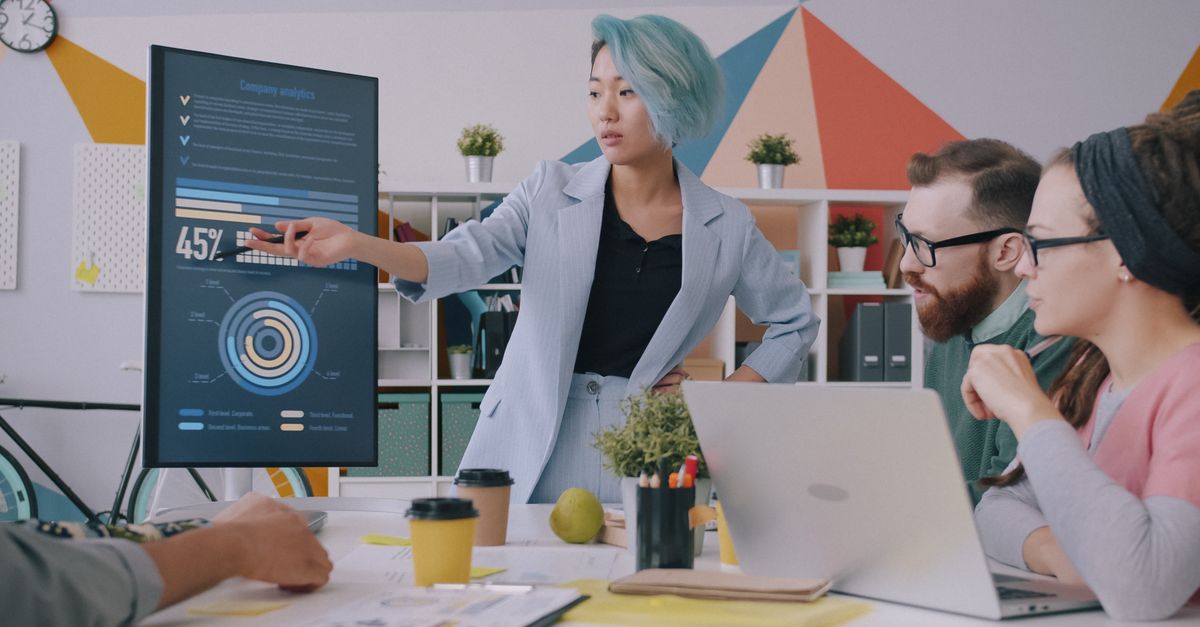 Diverse team meeting with data presentation on screen in modern office setting.