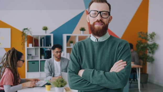 Portrait of a confident professional in a creative office environment with colleagues working in the background.
