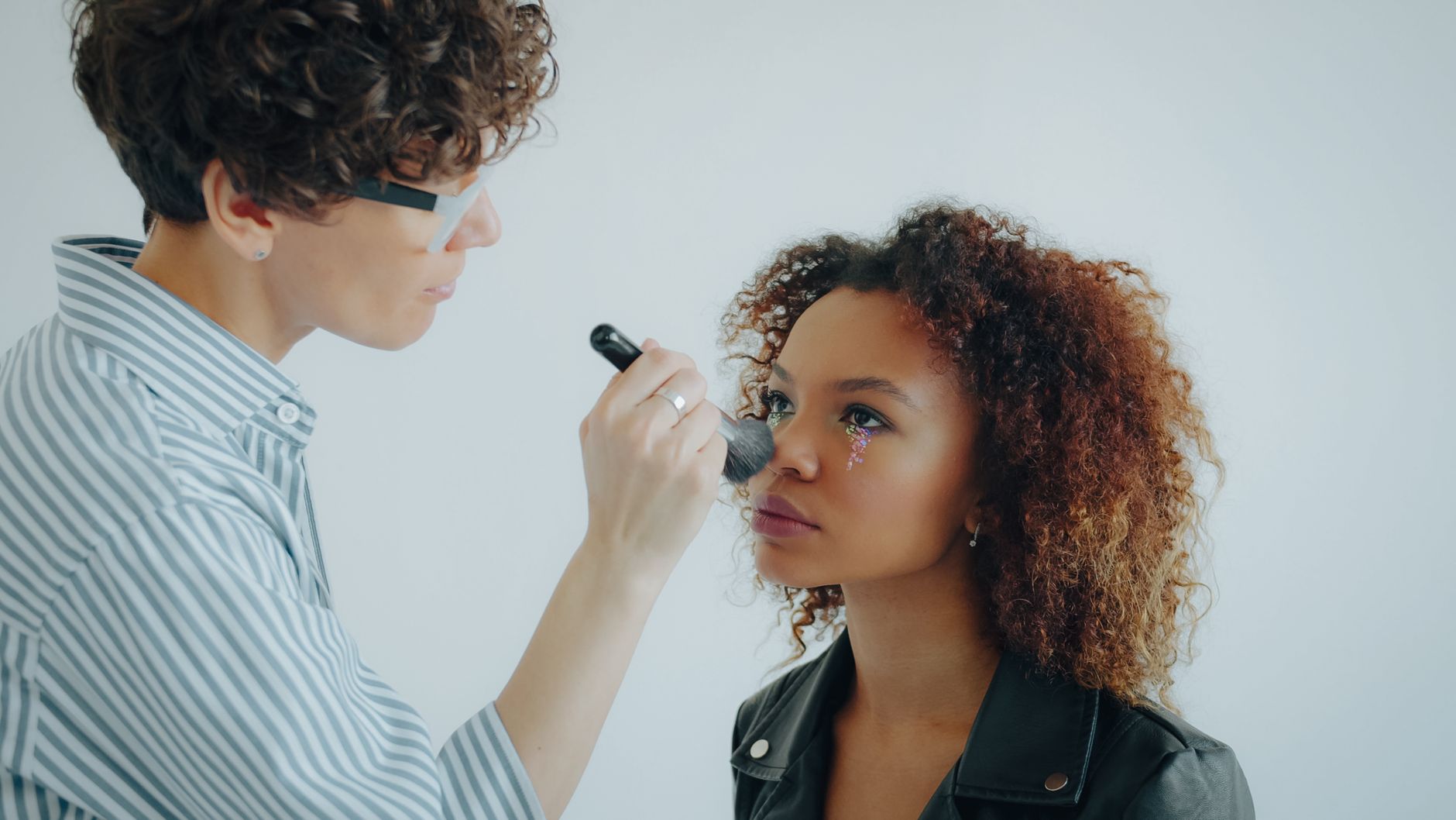 A makeup artist delicately applies blush to a model with floral eye art.