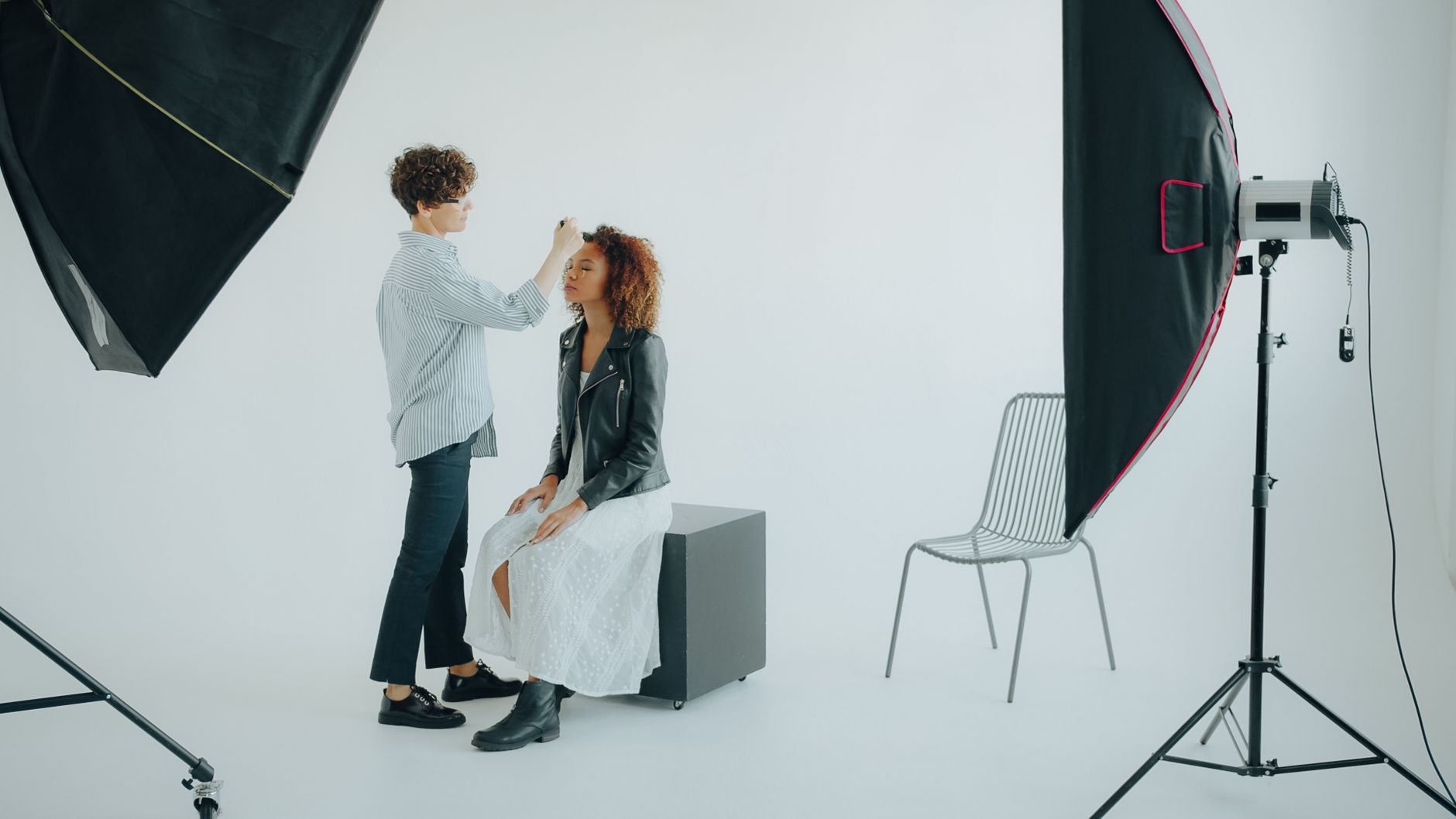 Makeup artist preparing model in a photography studio setup.
