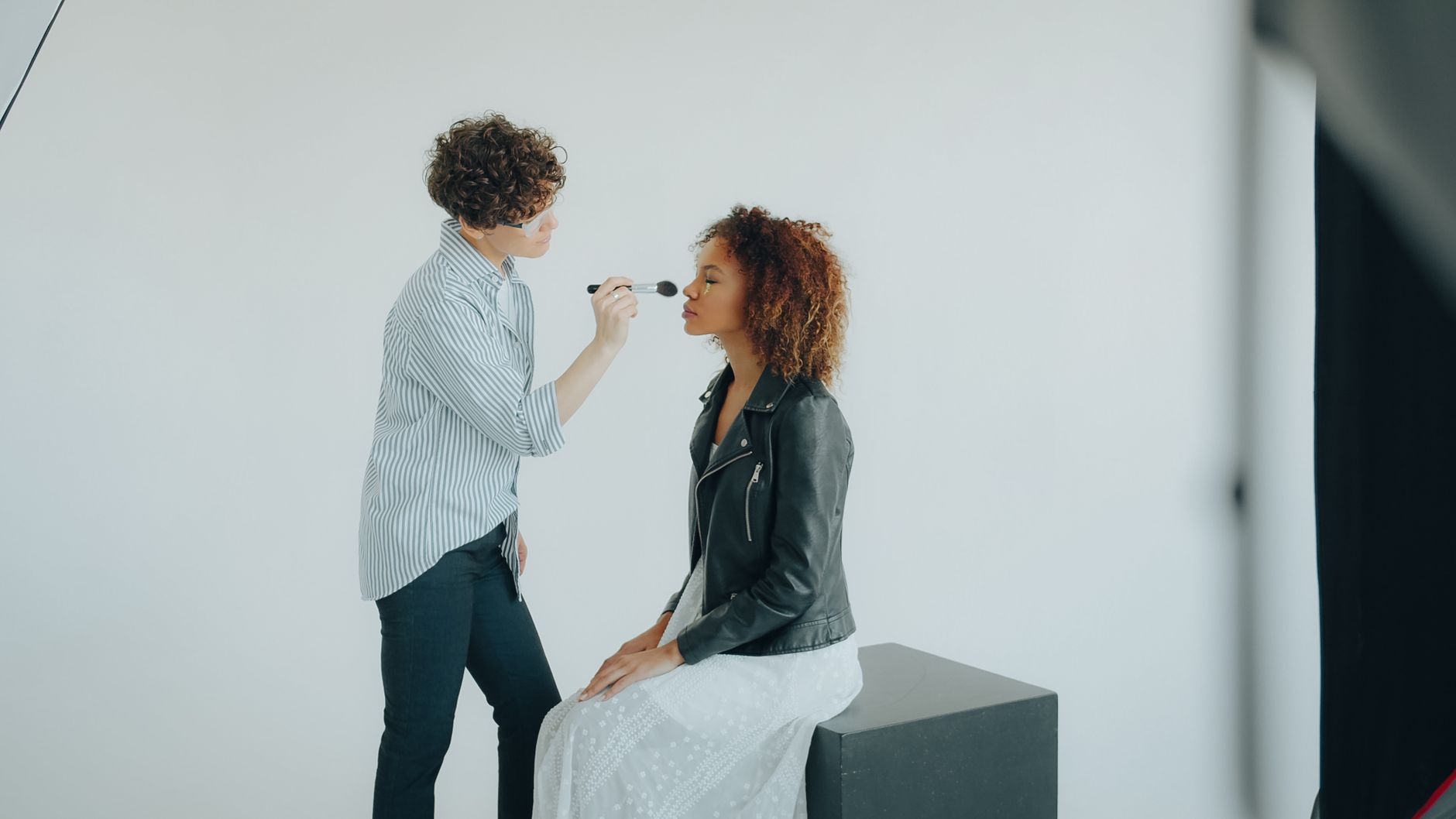 A makeup artist applies cosmetics to a woman in a studio setting.