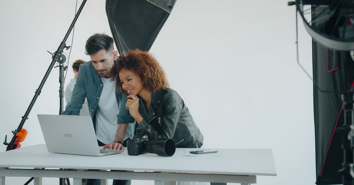 Two photographers reviewing work on a laptop in a professional studio setting.