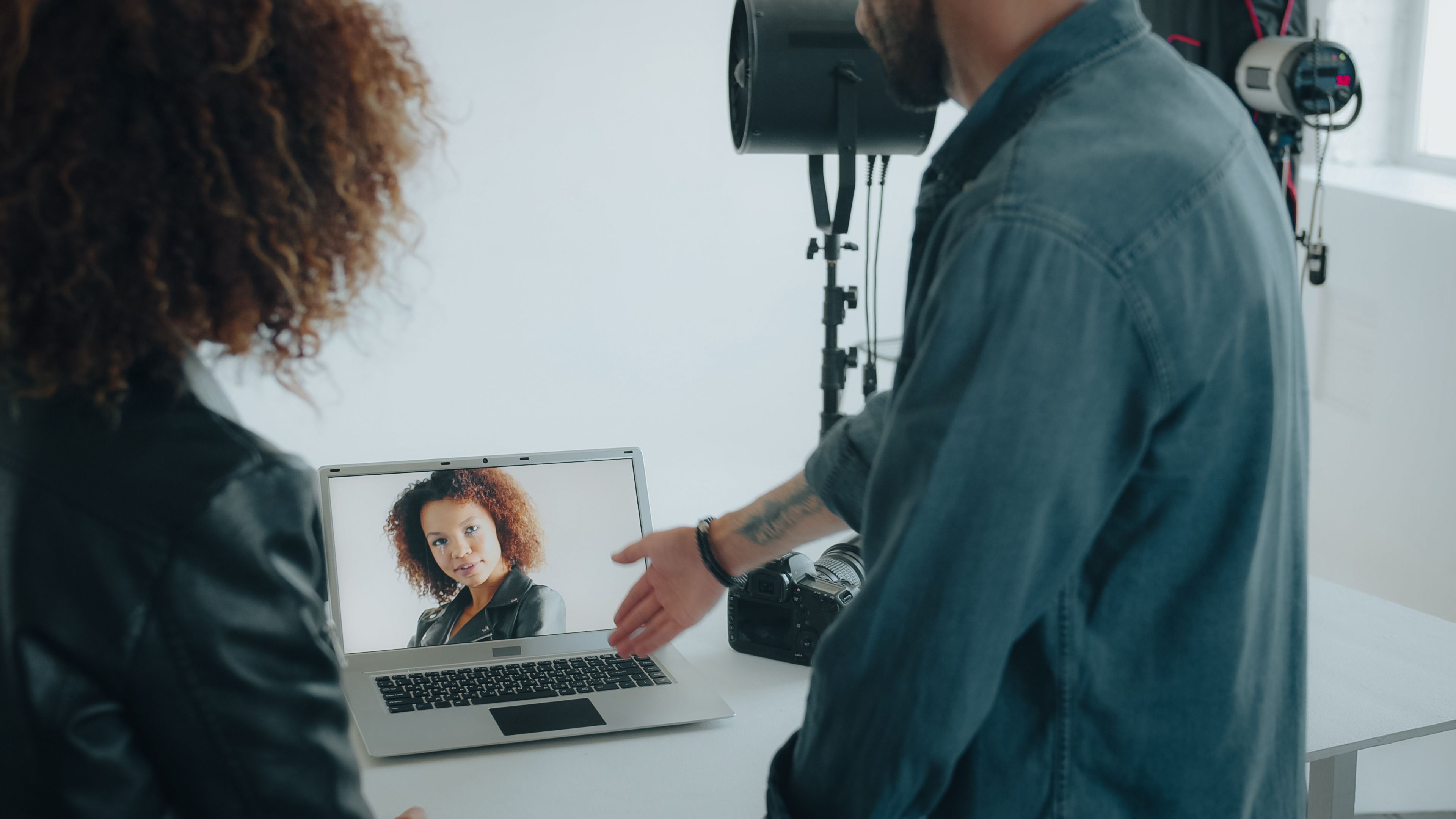 Photographer reviews a model's portrait on a laptop in studio setup, highlighting collaboration.