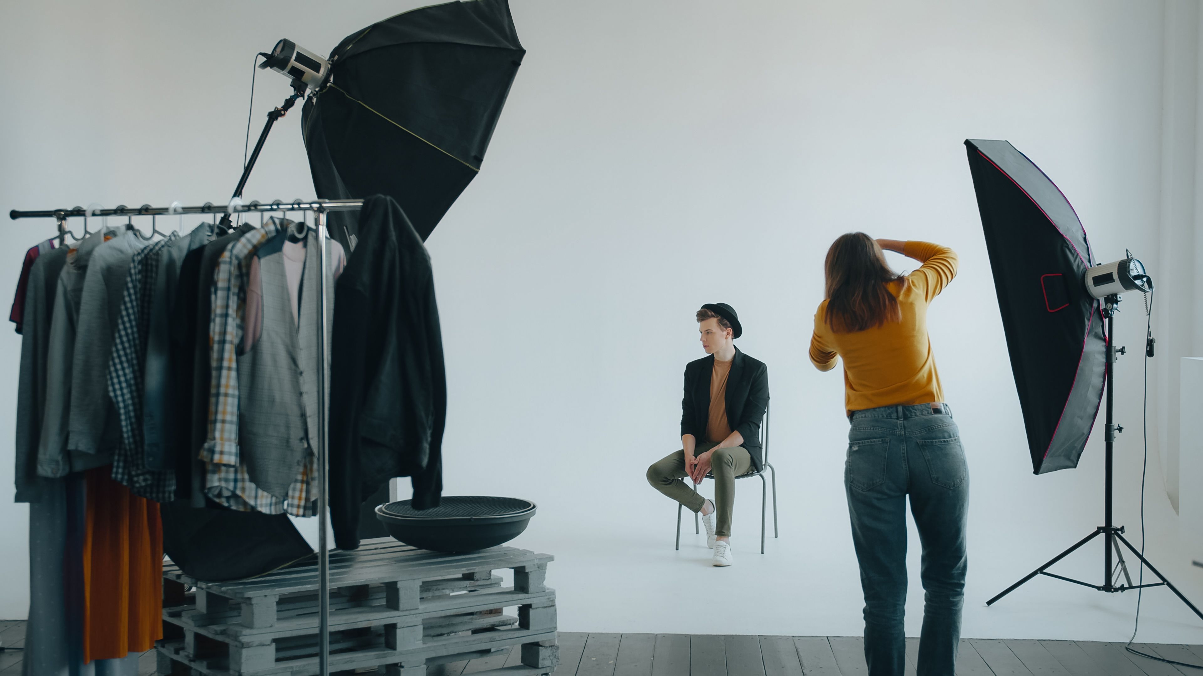 Modern studio fashion photoshoot featuring photographer and model with lighting setup.