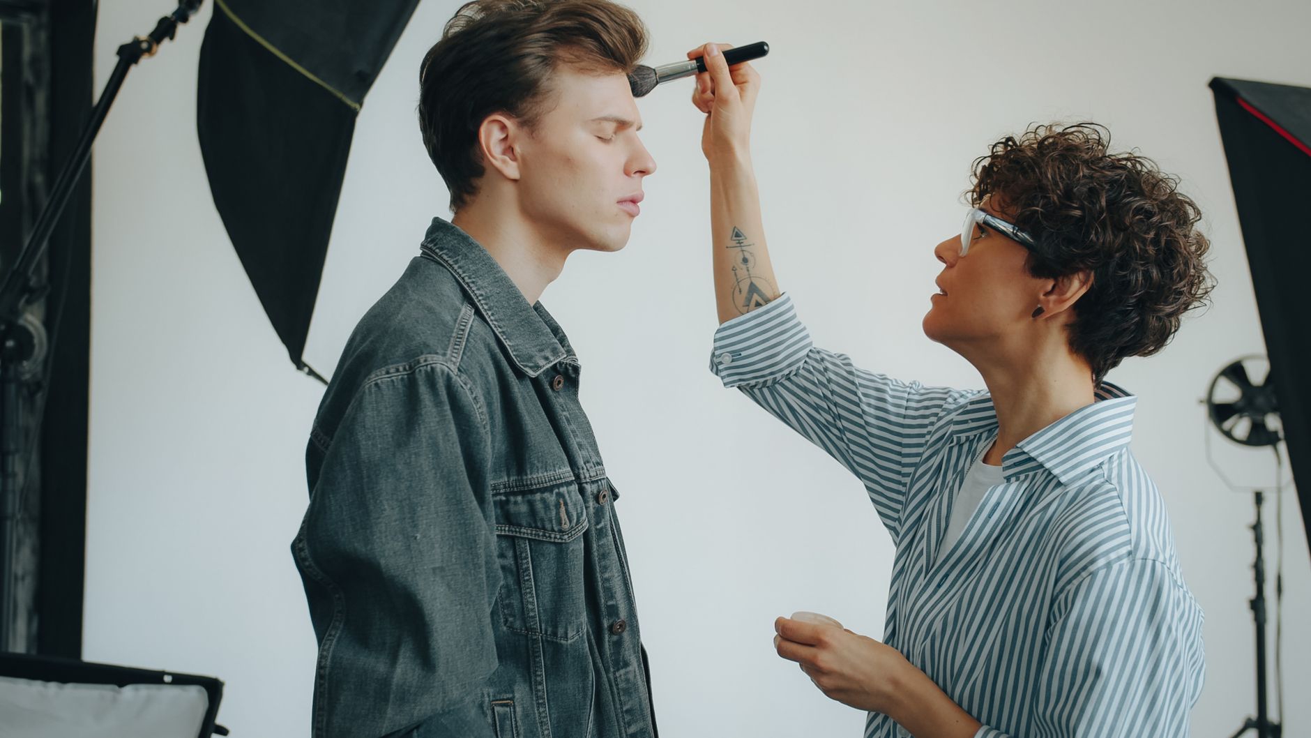 A makeup artist applies cosmetics to a model during a studio photoshoot session.