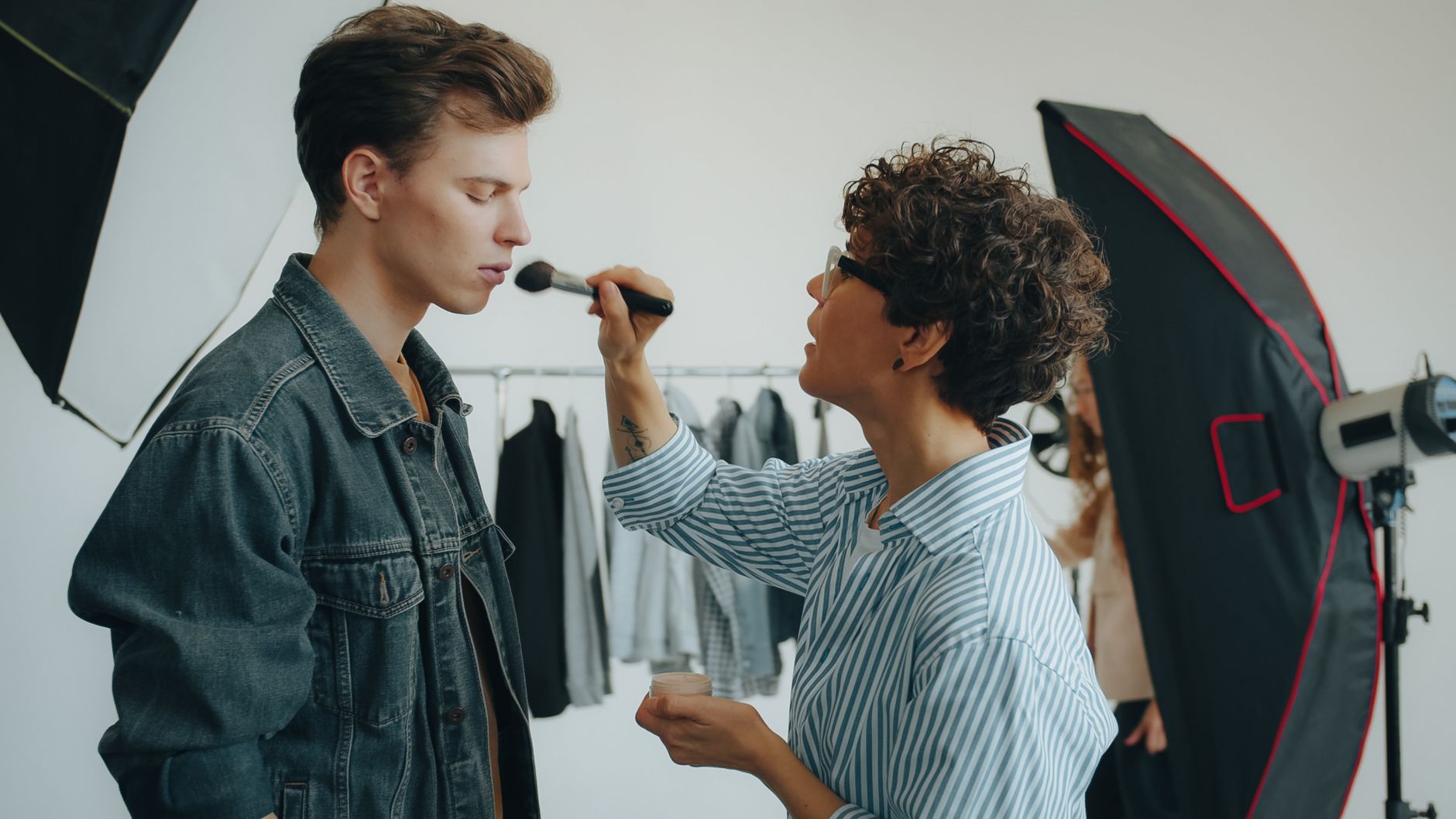 Makeup artist applying cosmetics on male model during a photoshoot in a studio setting.