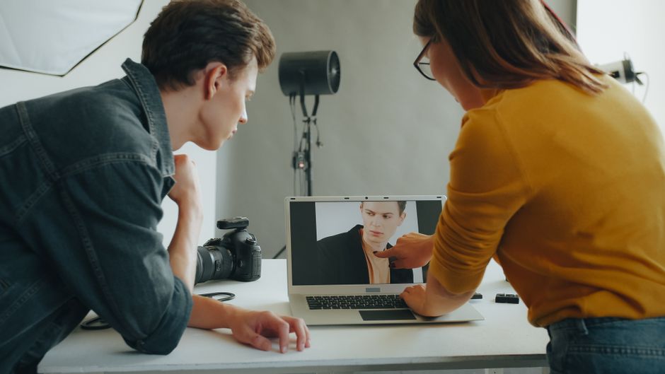 Two photographers review a portrait on a laptop during a studio session.