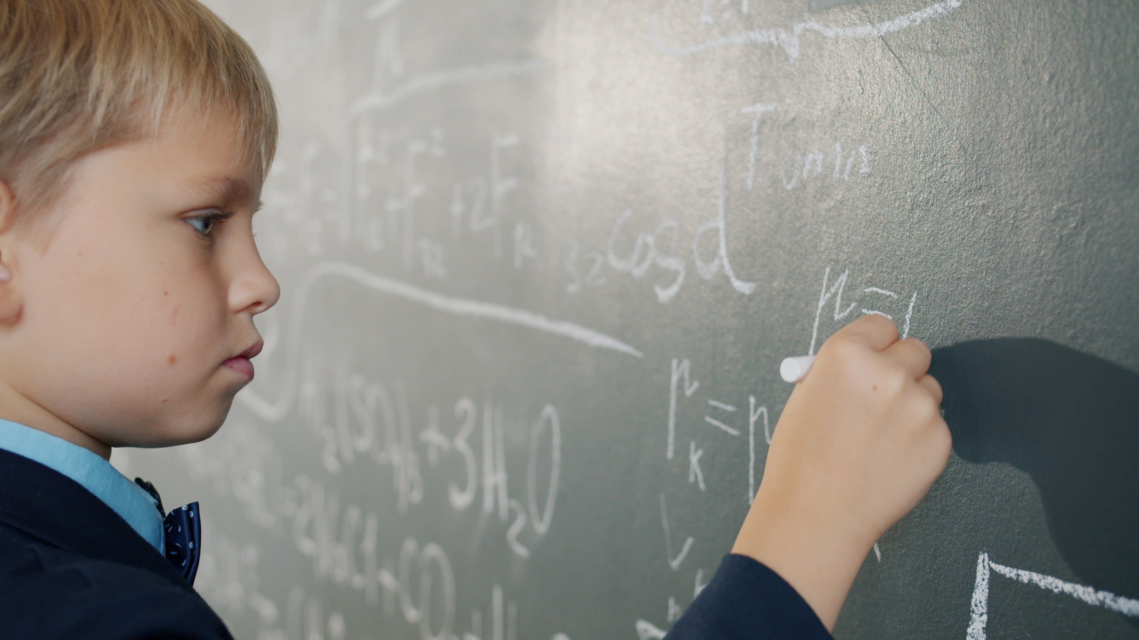 Young boy writing math equations on a classroom blackboard.