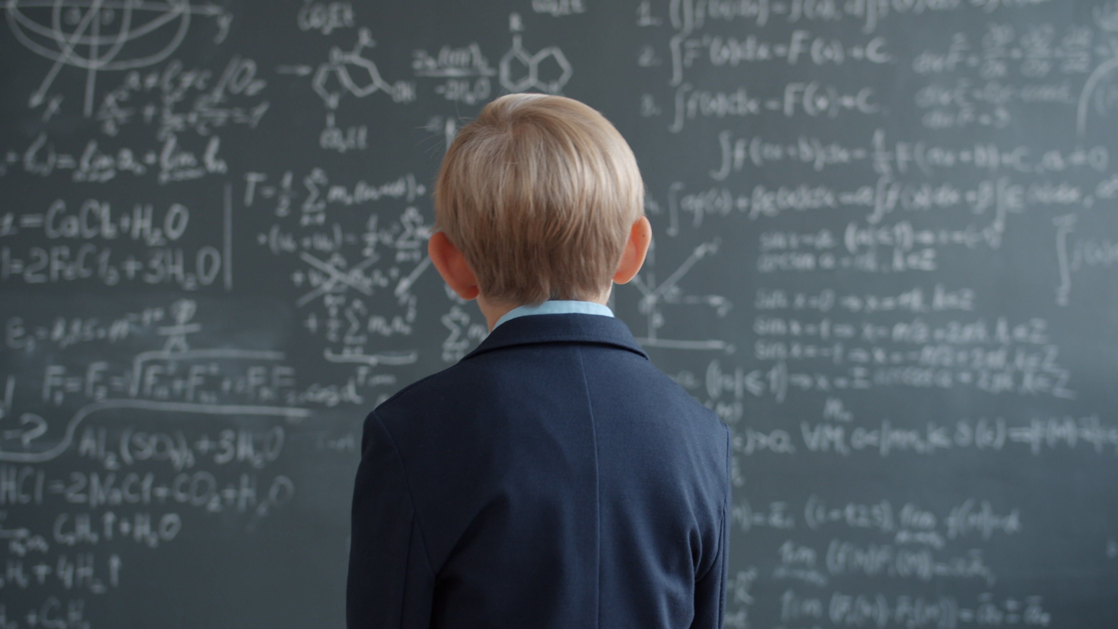 Child in school uniform studying complex math on chalkboard.
