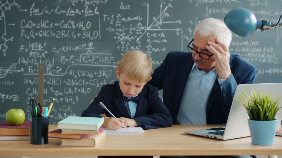 Elderly teacher helping a young student with homework in a classroom setting.