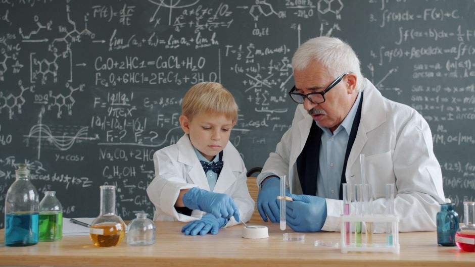 Young boy and elderly scientist working together in a chemistry lab.