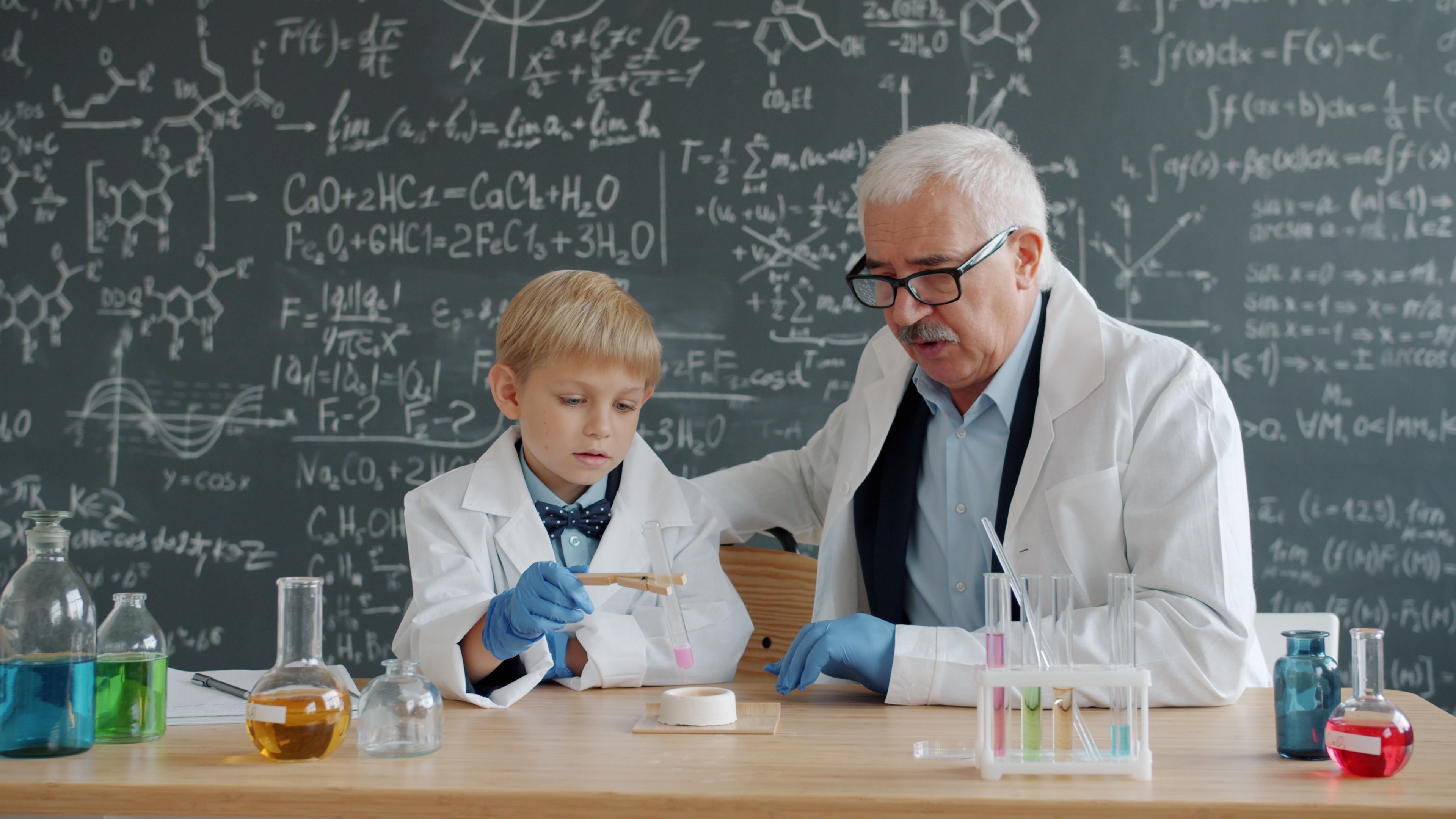Elder man and young boy in lab coats perform a chemistry experiment.
