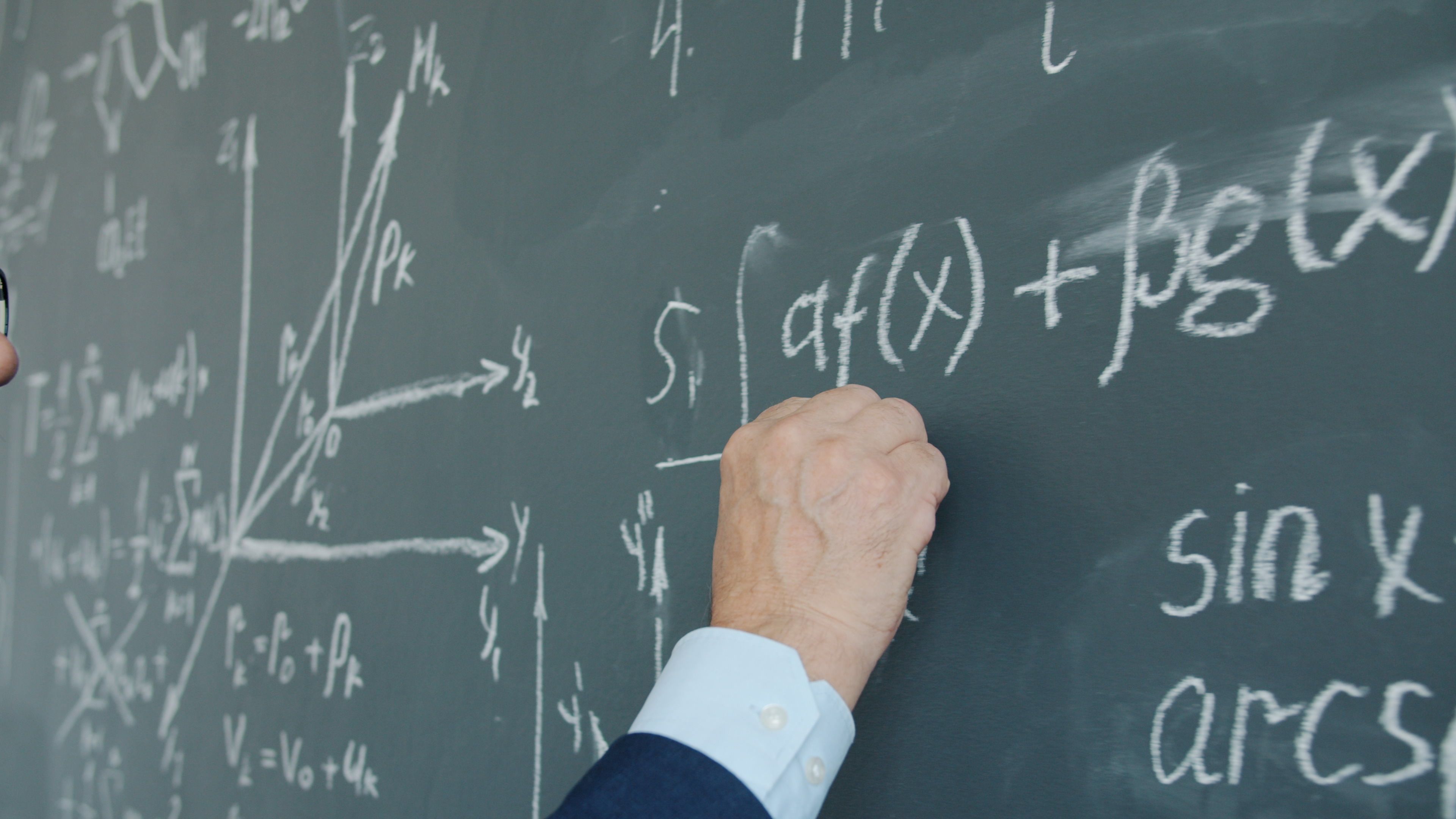 Close-up of a person writing complex mathematical equations on a chalkboard.