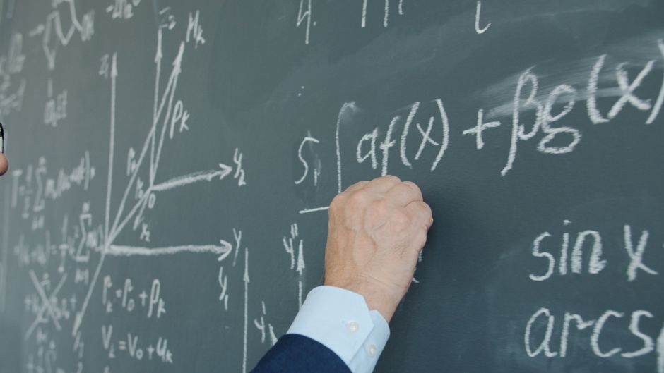 Close-up of a person writing complex mathematical equations on a chalkboard.