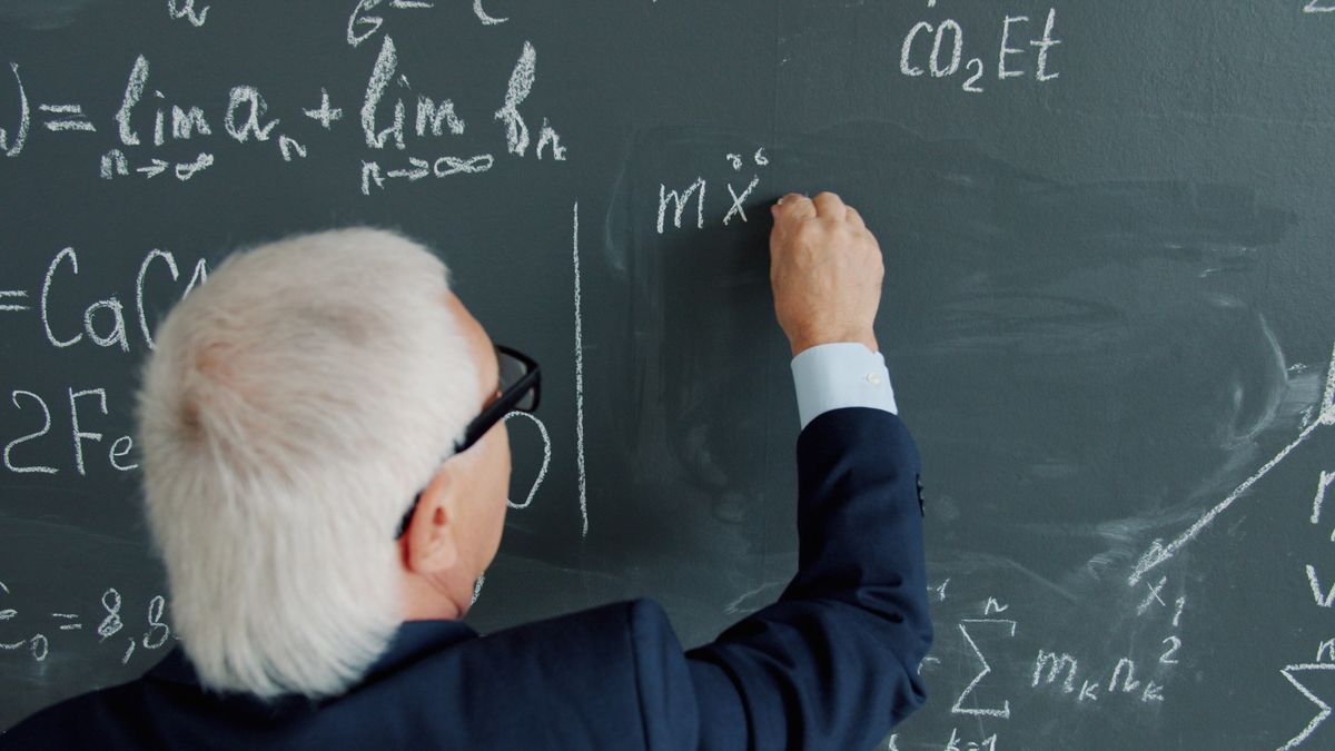A senior mathematics professor writing complex equations on a chalkboard, representing the human understanding mathematicians say the AI proof still lacks