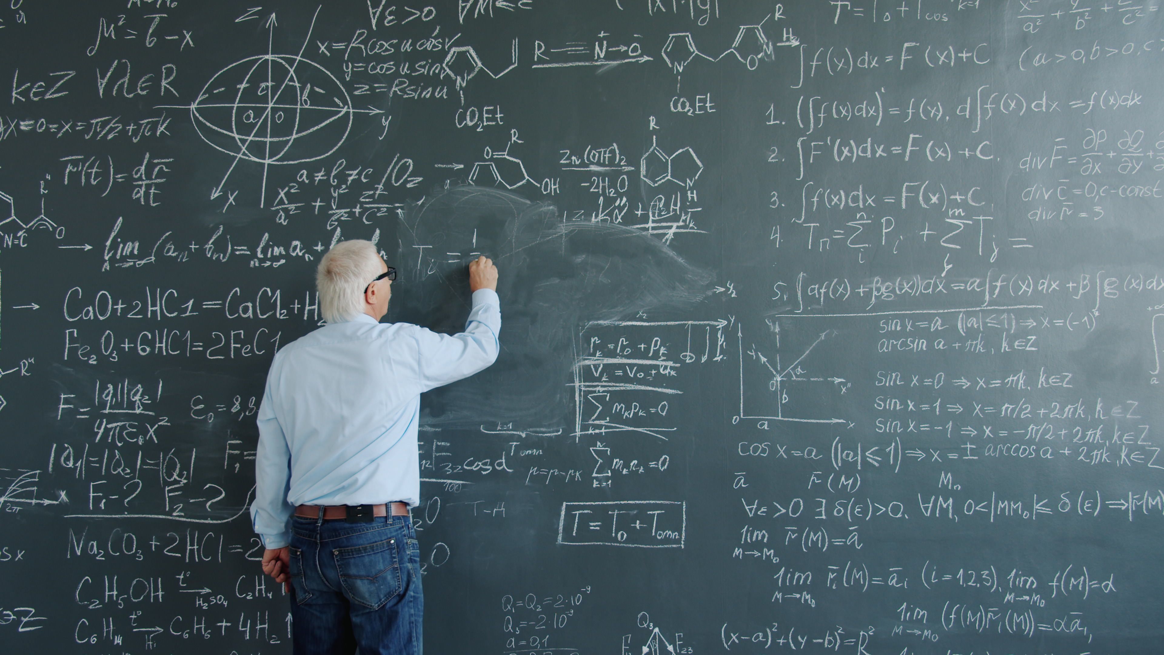 Senior scholar working out complex mathematical equations on a blackboard.