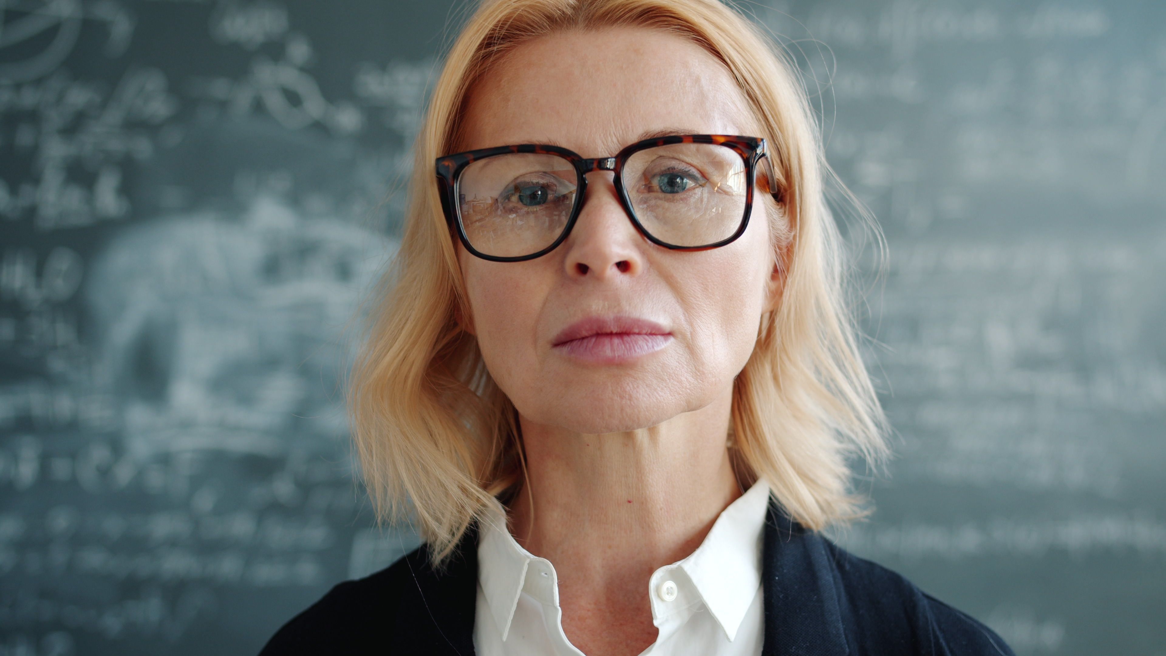 Portrait of a mature female teacher in front of a chalkboard, confident and focused.