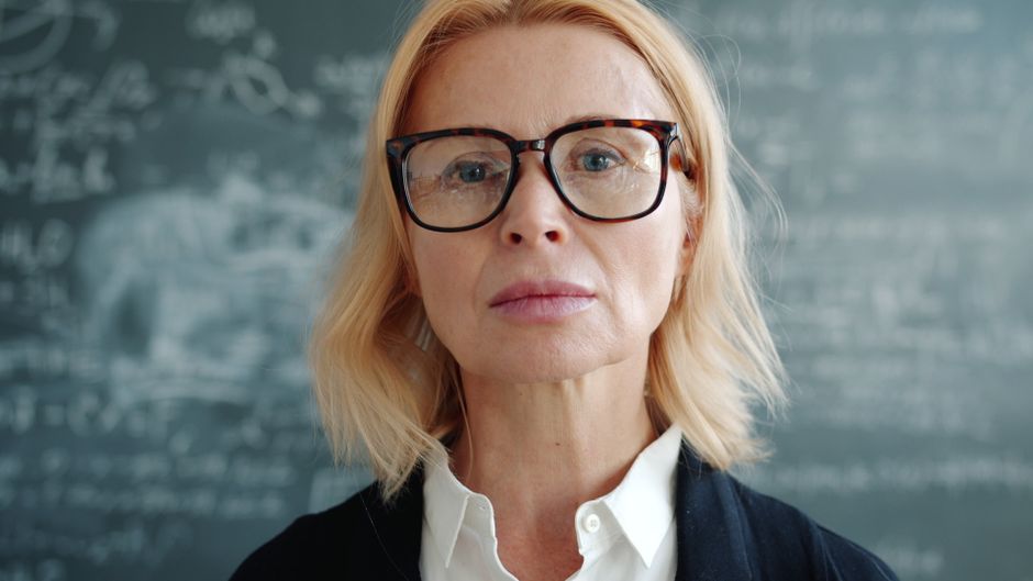 Portrait of a mature female teacher in front of a chalkboard, confident and focused.