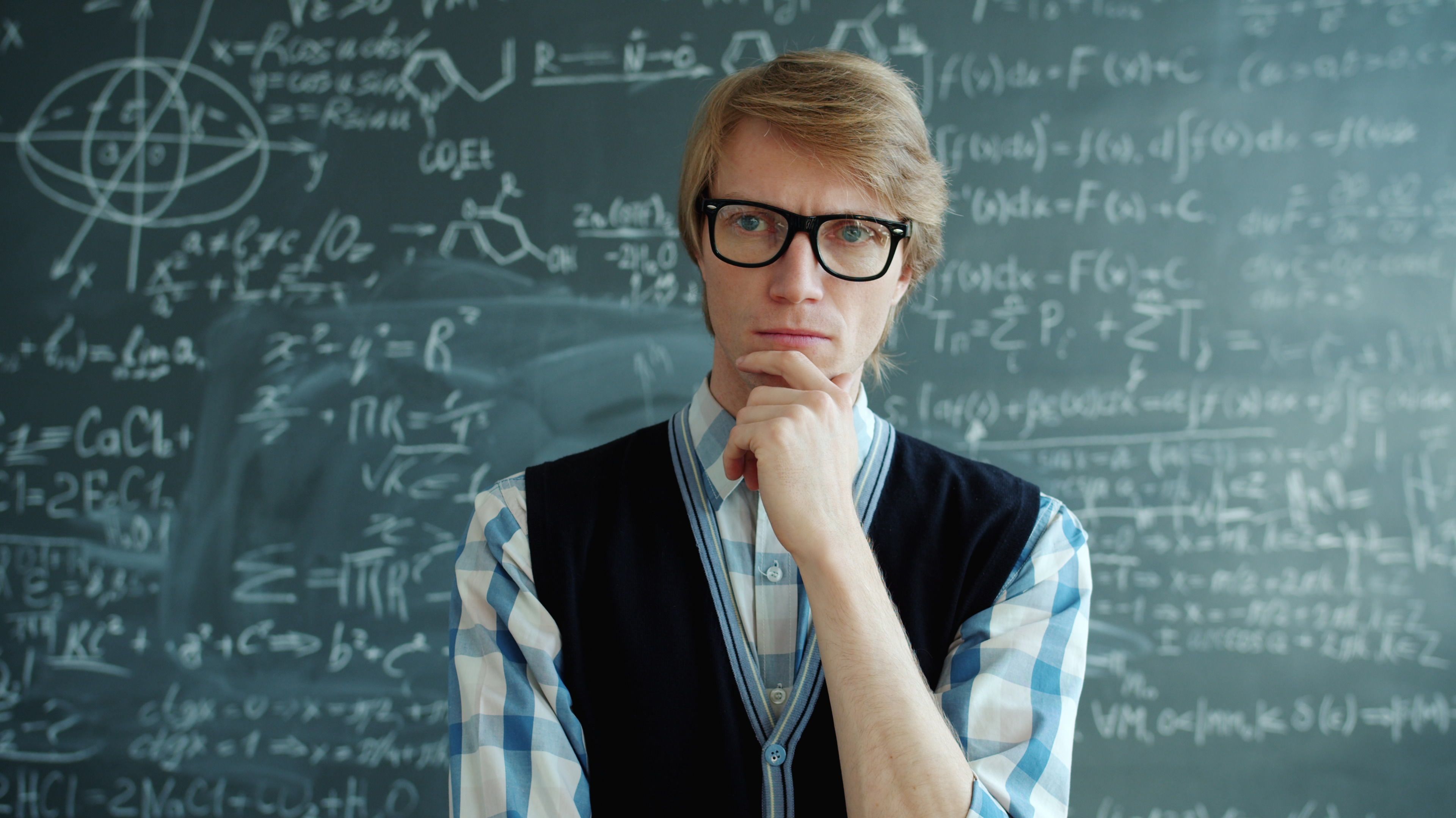 Thoughtful teacher pondering complex math equations on chalkboard.